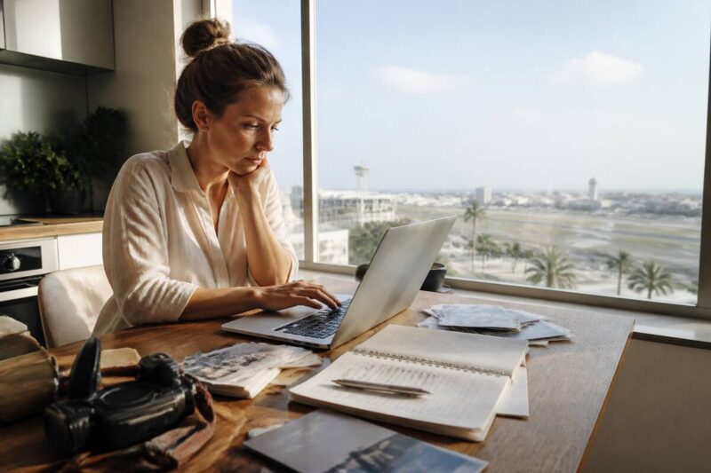 Iemand die vakantieaanbiedingen vergelijkt op een laptop met reisnotities op tafel